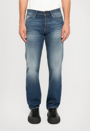Dark blue denim jeans with a faded finish, standard five-pocket design, and contrasting stitching details. Paired with black sneakers.