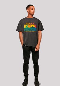 Dark gray cotton t-shirt with a colorful "Rocky Mountain National Park" graphic, complemented by black sweatpants and black athletic shoes.
