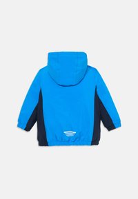 Blå og marineblå vindjakke med hette, elastiske mansjetter og en hvit buet detalj bak. Laget av lett, glatt materiale.