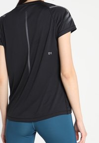 Schwarzes Sport-T-Shirt mit kurzen Ärmeln, reflektierenden Streifen und dem Label "D1" nahe dem Saum, hergestellt aus atmungsaktivem, feuchtigkeitsableitendem Stoff.