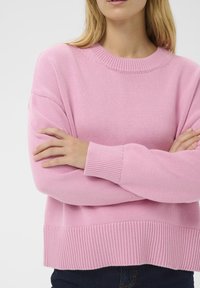 Pull rose tricoté avec un col et un ourlet côtelés. Il présente des manches longues et une coupe décontractée, confectionné dans un tissu doux.