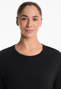 Black long-sleeve top with a rounded neckline and smooth, lightweight fabric. Close-fitting design contours to the body.