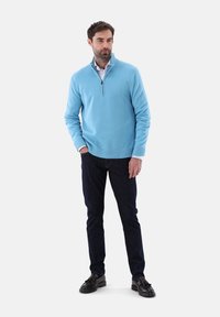 Helles blauer Zip-Kragen-Pullover aus weichem Strickstoff, kombiniert mit dunkelblauen Jeans und schwarzen Schuhen, mit gerippten Bündchen und Saum.