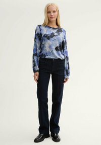 Camicia a maniche lunghe blu e nera a fantasia, abbinata a jeans a zampa d'elefante in denim scuro. La camicia ha una vestibilità comoda; i jeans presentano tasche frontali.