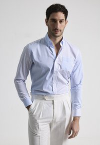 Camisa abotonada de rayas azul claro con un bolsillo, corte ajustado, combinada con pantalones blancos con pliegues. Tejido de algodón suave, de mangas largas.