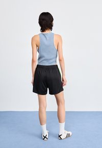 Blå ribbet tank topp, sorte shorts med neongrønn side stripe, ankel sokker og slip-on sko med svart og hvitt design.
