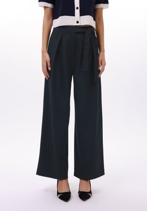 Pantalons à jambes larges en tissu vert foncé, dotés d'une ceinture à nouer à la taille, avec une texture lisse et un design fluide.
