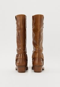 Bottes en cuir marron jusqu'au genou avec un design décontracté, présentant des accents à pression, un talon bas et une texture lisse. Marquées "REPLAY" sur le côté.