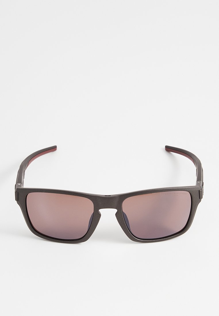 Schwarze rechteckige Sonnenbrille mit dunkel getönten Gläsern und geraden Bügeln, auf einem weißen Hintergrund in frontalem Blickwinkel dargestellt.