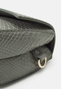 Borsa a tracolla grigia con motivo serpente, dalla superficie testurizzata e con hardware dorato. Presenta un dettaglio a patta ripiegata e un anello metallico rotondo.