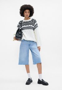 Valge kaeluskudumine, millel on must mustriga yoke, helesinised denim culotte püksid, must kott, mustad loafers kingad ja valged sokid.