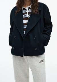 Granatowy płaszcz podwójnie zapinany z miękkiego materiału z dużymi klapami, w połączeniu z paskowanym polo i szarymi spodniami dresowymi z logo "santa monica".