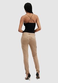 Beige cargobyxor med sidoknappar, fransad fåll och fickor. Bärs med en åtsittande svart topp. Höga klackar fulländar looken.