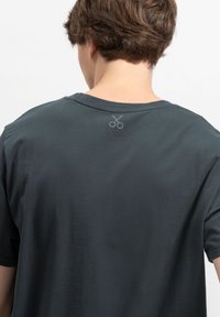 Donkergrijze T-shirt met korte mouwen en een ronde halslijn. Heeft een subtiele schaarafbeelding gedrukt op het achterste deel van de hals. Zachte textuur.