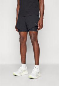 Șorturi atletice negre cu căptușeală interioară, cu un tiv curbat și un logo. Adidași albi cu accente verzi și tălpi texturate.