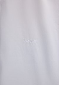 Witte stoffen shirt met een gladde textuur; voorzien van geborduurd "JOOP!" logo in subtiele witte draad, centraal op de voorkant geplaatst.