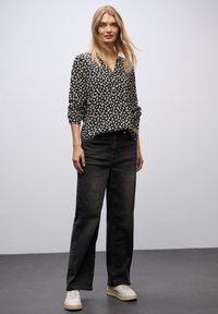 Sort og hvid mønstret bluse med V-udskæring, lange ærmer, paired med høj talje mørke jeans og hvide sneakers. Minimalistisk design.