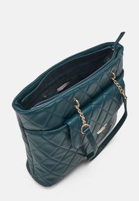 Teal quiltad handväska med en strukturerad design, guldkedjeaccenter, dragkedjeslutning upptill och ett innerfack. Slät lädertextur.
