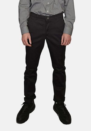 Pantaloni neri slim fit in tessuto tessuto, caratterizzati da un classico design a cinque tasche, abbinati a scarpe sportive nere.