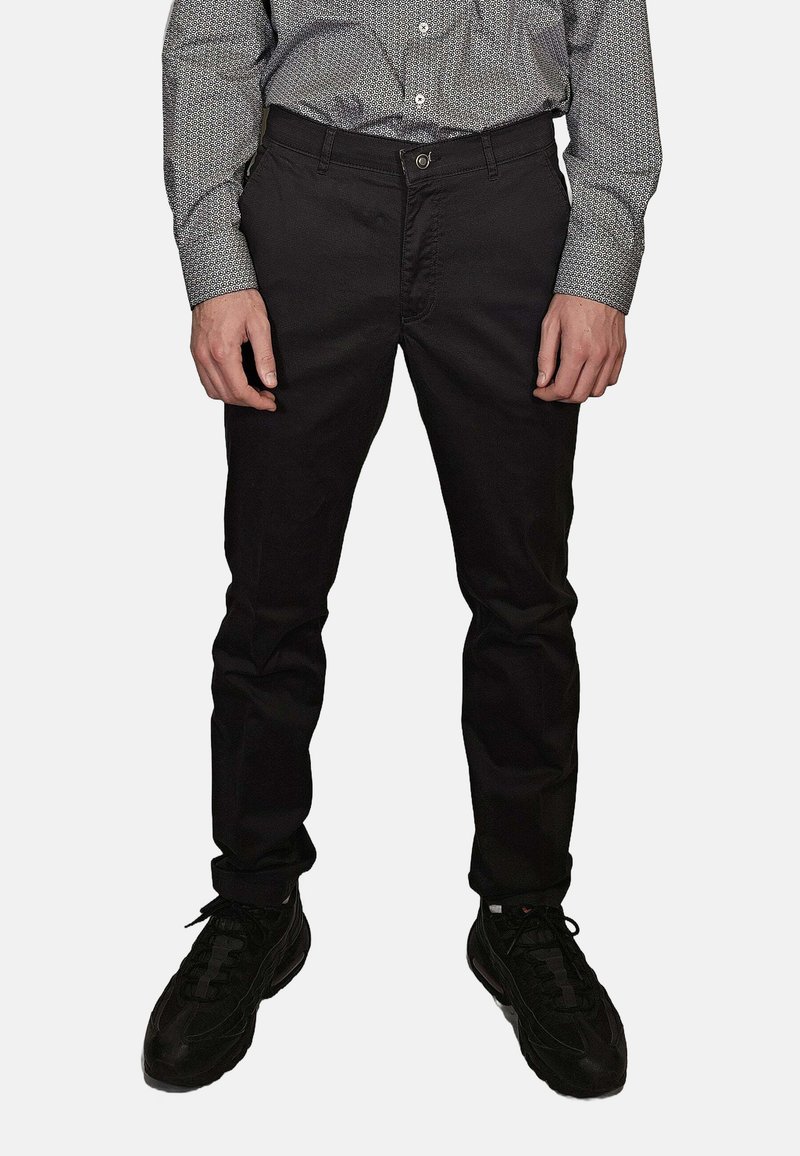 Pantaloni neri slim fit in tessuto tessuto, caratterizzati da un classico design a cinque tasche, abbinati a scarpe sportive nere.