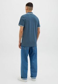 Polo shirt in donkerblauwe katoen met korte mouwen, met gestreepte kraagaccenten. Draag het met lichtblauwe baggy jeans en witte sneakers.