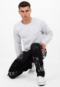 Felpa grigia abbinata a pantaloni neri con toppe, tessuto strutturato e accenti rossi. Sneakers bianche con rifiniture rosse completano il look.