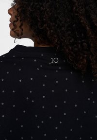 Sort t-shirt med sølvprikker, rund halsudskæring og et lille "10" broderet på ryggen. Blødt bomuldsstof med en glat tekstur.