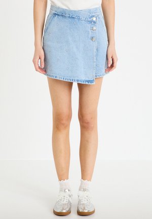 Lyseblå denim slå-om nederdel med små hvide blomsterbroderier og sølvknapper, båret med hvide sokker og metalliske sølv sneakers.