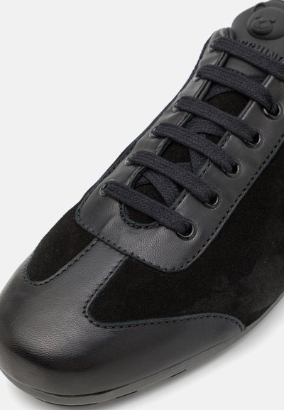 Black sneaker with a mix of smooth leather and suede. Features rounded toe, flat laces, and stitched accents on the upper.
