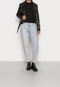 Czarna skórzana kurtka motocyklowa, ciemny sweter dzianinowy z beaded wzorem, jasnoniebieskie zniszczone dżinsy, czarne botki z klamrami.