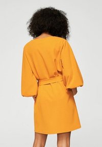 Sukienka z krótkim rękawem w intensywnym pomarańczowym kolorze, z podkreśloną talią za pomocą paska, teksturowanym materiałem oraz luźnym, swobodnym krojem.