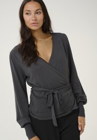 Gray wrap top with long sleeves, featuring a deep V-neck and tied waist. Soft fabric and ribbed cuffs accentuate the relaxed design.