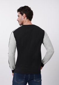 Crna i siva majica dugih rukava s kontrastnim rukavima, okruglim izrezom i crnim manžetama. Glatki materijal s minimalnim detaljima.