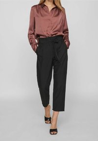 Sidenblus i mauve med knappstängning framtill och långa ärmar, kombinerad med svarta högmidjade byxor och svarta klacksandaler.