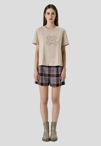 Beige cropped t-shirt met geborduurd ontwerp, gecombineerd met geruite shorts in donkerrood, blauw en wit. Grijze enkellaarsjes maken de look compleet.
