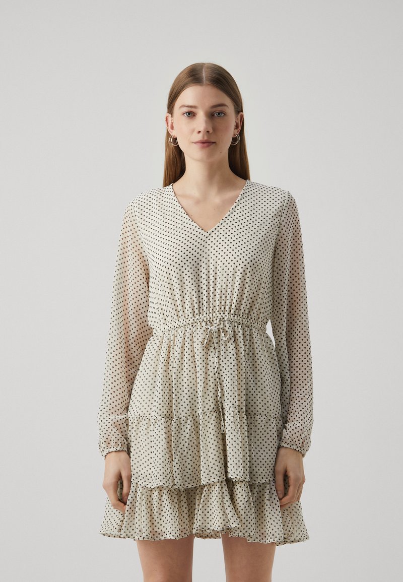 Φως, διάφανο φόρεμα με V-λαιμόκοψη, ελαστική μέση, μακριά μανίκια και tiered ρίγες. Διαθέτει μικρές μαύρες βούλες σε κρεμ φόντο.