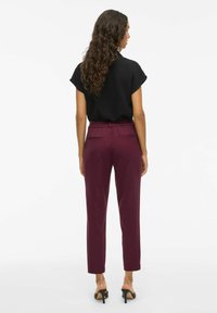 Bordeaux tapered broek met een elastische taille, twee achterzakken en een gladde stofafwerking, gecombineerd met een zwart shirt met korte mouwen.