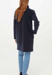 Abrigo de lana azul marino con cuello alto, mangas largas y bolsillos laterales; presenta una superficie ligeramente texturizada y un diseño hasta la rodilla.