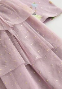 Tulle rose translucide superposé avec des pois dorés. Dispose d'une texture douce et fluide ainsi que de détails en volants délicats. Accents de motifs floraux subtils.
