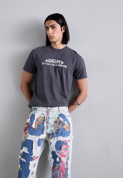 Gray cotton t-shirt with a white graphic print. Distressed white denim pants with colorful patchwork and frayed edges.
