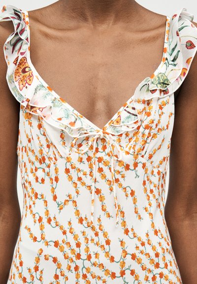 Κοντινό πλάνο ενός λευκού αμάνικου φορέματος με πορτοκαλί ανθικό σχέδιο και βολάν στη λαιμόκοψη, δεμένο με μικρό φιόγκο στο κέντρο.