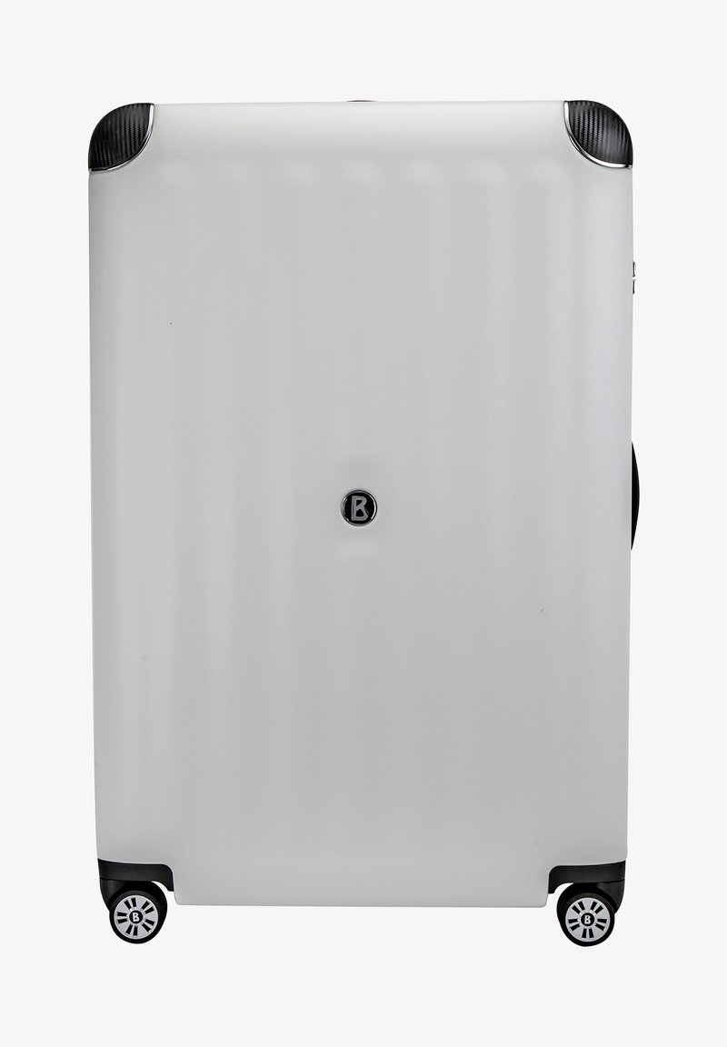 Maleta rígida, cuerpo blanco, acentos negros en las esquinas y ruedas, textura suave, logo en el centro, cuatro ruedas para movilidad.