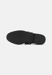 Încălțăminte neagră cu o talpă din cauciuc texturat, având un design plat și curele minimaliste pe partea superioară pentru o ajustare sigură.