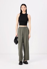 Haut court noir sans manches associé à un pantalon ample vert olive, portant un sac à main noir. Des chaussures plates noires complètent la tenue.