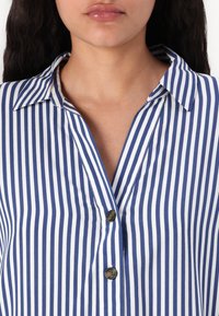 Blue and white striped button-up shirt with a collared neckline, featuring a V-shaped opening and dark buttons on the front placket.