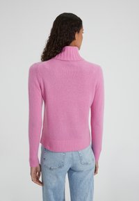 Maglione rosa a collo alto con polsini e orlo a costine, realizzato in materiale morbido, mostrato da dietro su uno sfondo neutro.