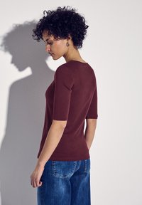 Burgundowy dopasowany top z krótkimi rękawami, gładka tekstura, okrągły dekolt w połączeniu z niebieskimi spodniami typu wide-leg, widok z tyłu.