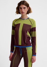 Langærmet atletisk top i grøn og burgunder med stribede detaljer, med rund halsudskæring og ribbet tekstur, kombineret med matchende tætsiddende leggings.