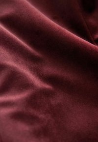 Bordowy materiał o miękkiej, teksturowanej powierzchni, z subtelnymi zagnieceniami i lekko błyszczącym wykończeniem, sugerującym luksusową jakość.