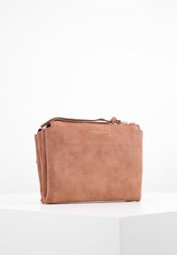 Zarte rosa Wildledertasche mit Reißverschluss, die ein minimalistisches Design und ein geprägtes Logo aufweist. Glatte Textur und rechteckige Form.